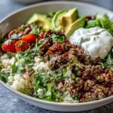 Steaming Low Carb Burrito Bowl with savory beef, fluffy cauliflower rice, fresh tomatoes, and a dollop of sour cream on a plate. 