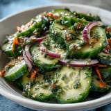 A chilled bowl of Refreshing Crunchy Cucumber Salad with julienned carrots and sesame seeds, ready to serve as a crisp, light side dish.