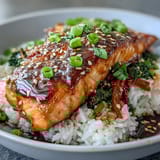 A close-up of a teriyaki salmon bowl shows tender fish, colorful broccoli, carrots, and snap peas for a satisfying weeknight meal.