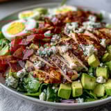Classic American Cobb Salad Bowl features hard-boiled egg quarters, juicy tomatoes, and a drizzle of tangy ranch dressing.  