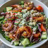 A close-up of a Greek Shrimp Bowl reveals a zesty lemon-olive oil dressing drizzled over the fresh ingredients.  