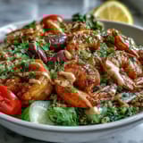 Freshly cooked Mediterranean Shrimp Bowl served in a white bowl, featuring red onion, olives, and lemon wedges for a zesty garnish.