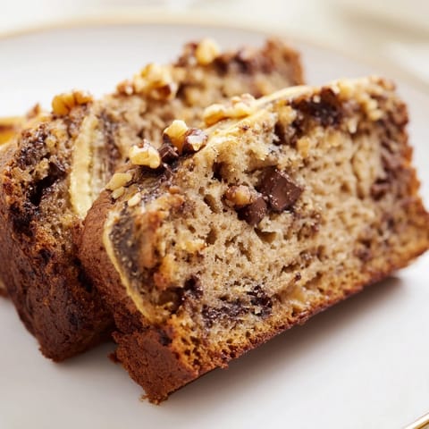 Golden-brown Banana Bread loaf cooling on a wire rack with melted butter and sliced bananas nearby.