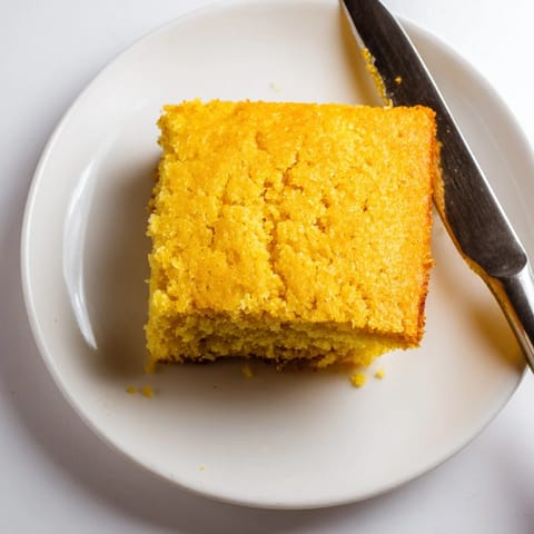 Freshly baked Cornbread in a cast-iron skillet, featuring a golden-brown, crispy crust and tender interior, served warm ready for butter.