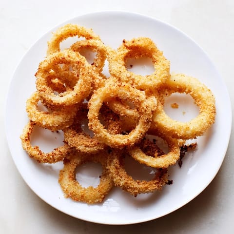 Deep-fried, golden onion rings piled high on a white plate with a small ramekin of creamy ranch dipping sauce. 