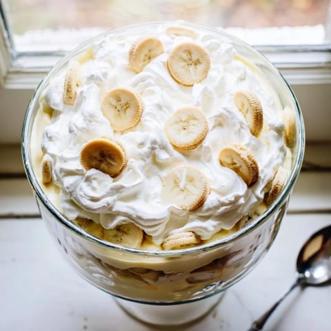 A classic Southern Banana Pudding topped with fluffy whipped cream, served in a glass trifle dish.