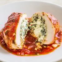 Golden-baked Spinach Ricotta Stuffed Chicken breasts resting in a rich, chunky tomato sauce, garnished with fresh basil leaves.