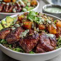 Roasted butternut squash steak bowls with quinoa, greens, and avocado on a rustic wooden table.