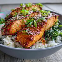 Steaming jasmine rice and sautéed spinach create a vibrant base for glazed salmon, garnished with green onions and sesame seeds.