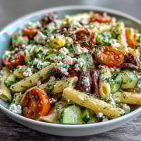Fresh summer pasta salad with Greek olives and feta, bursting with juicy tomatoes and crisp cucumbers in a tangy herb dressing.